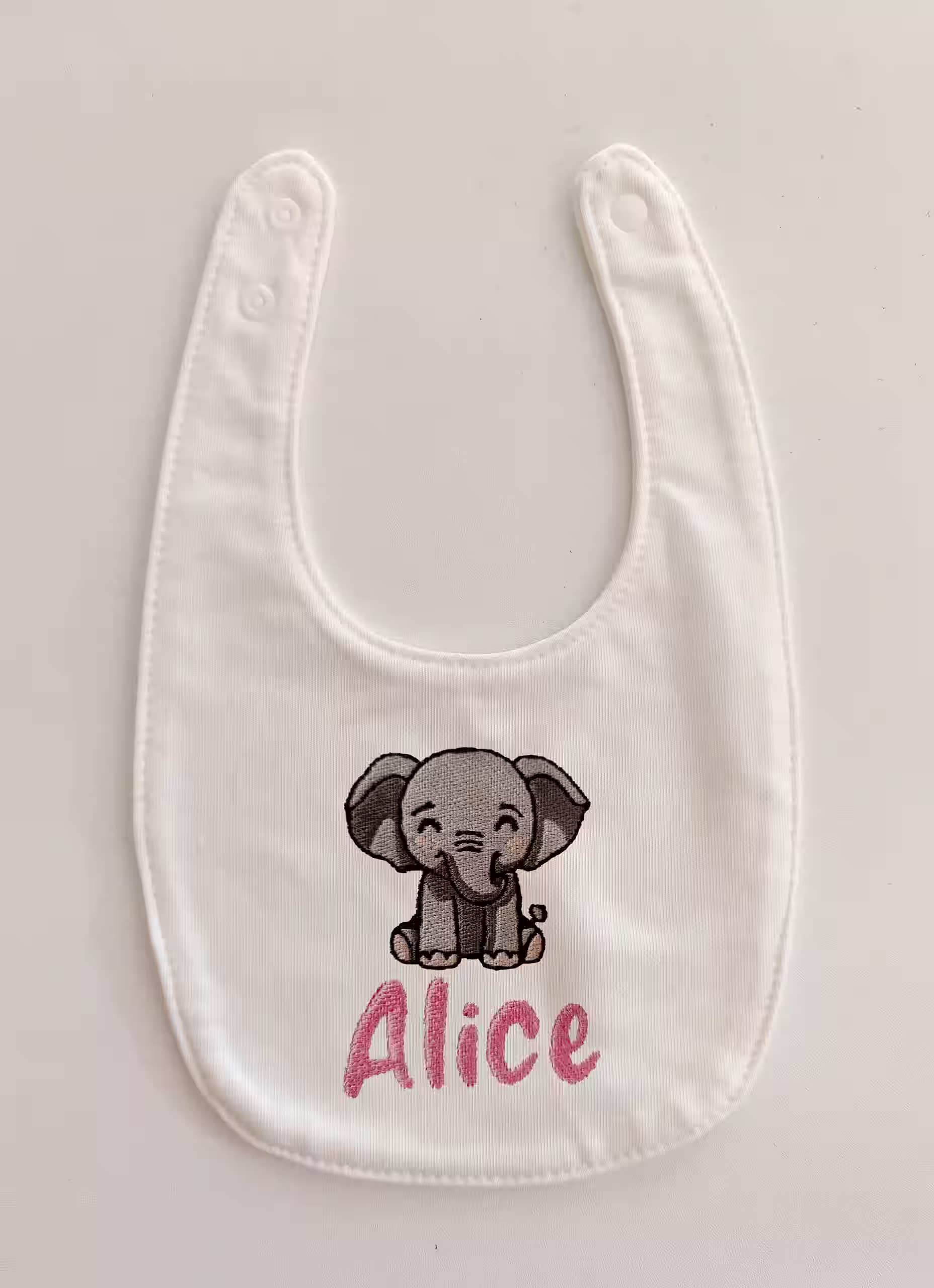 Fotografia di un bavaglino per neonato personalizzato con ricamato il nome "Alice" in rosa in basso e sopra un elefantino.